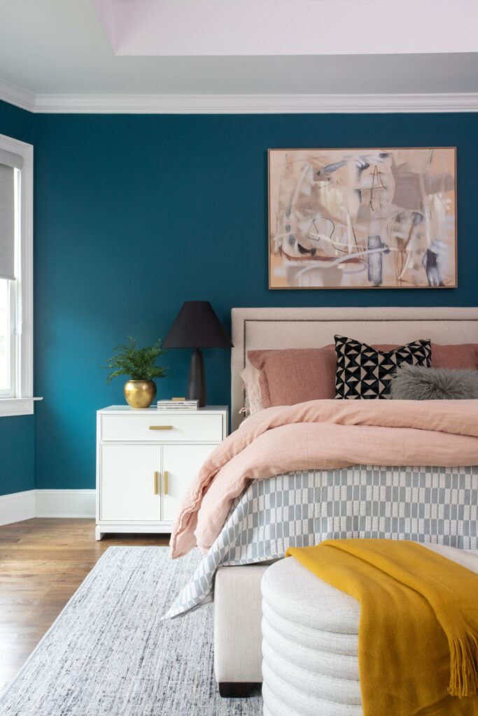 Bedroom with blue wall and bed with pink, gray, black, and white comforters and pillows. 
