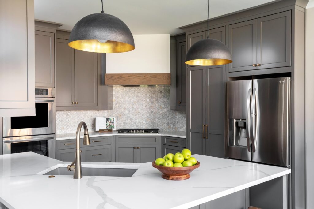 Kitchen with gray pendant lights, gray cabinets, and speckled tile backsplash.