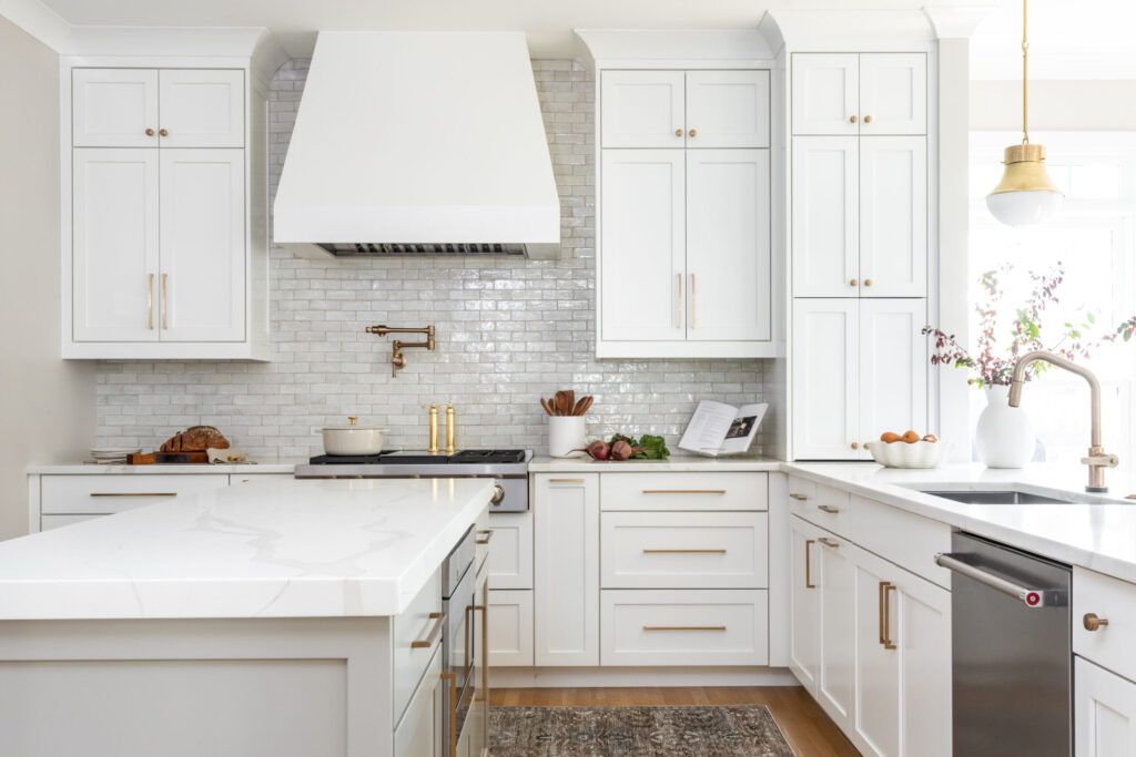 Kitchen with white cabinets and hood and gold hardware. 
