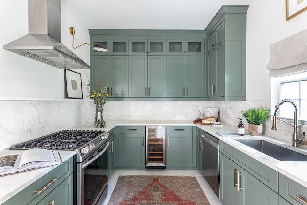 Kitchen with green cabinets and marble countertops and backsplash.