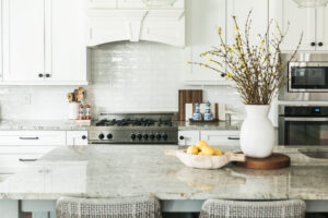 A bright kitchen we intricate kitchen hood, plain vase, and marble countertop.