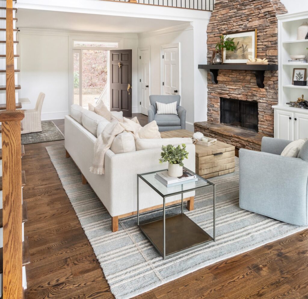 Cozy living room with a stone fireplace, neutral sofa, and two armchairs, creating a warm and inviting seating area with a mix of rustic and contemporary elements.