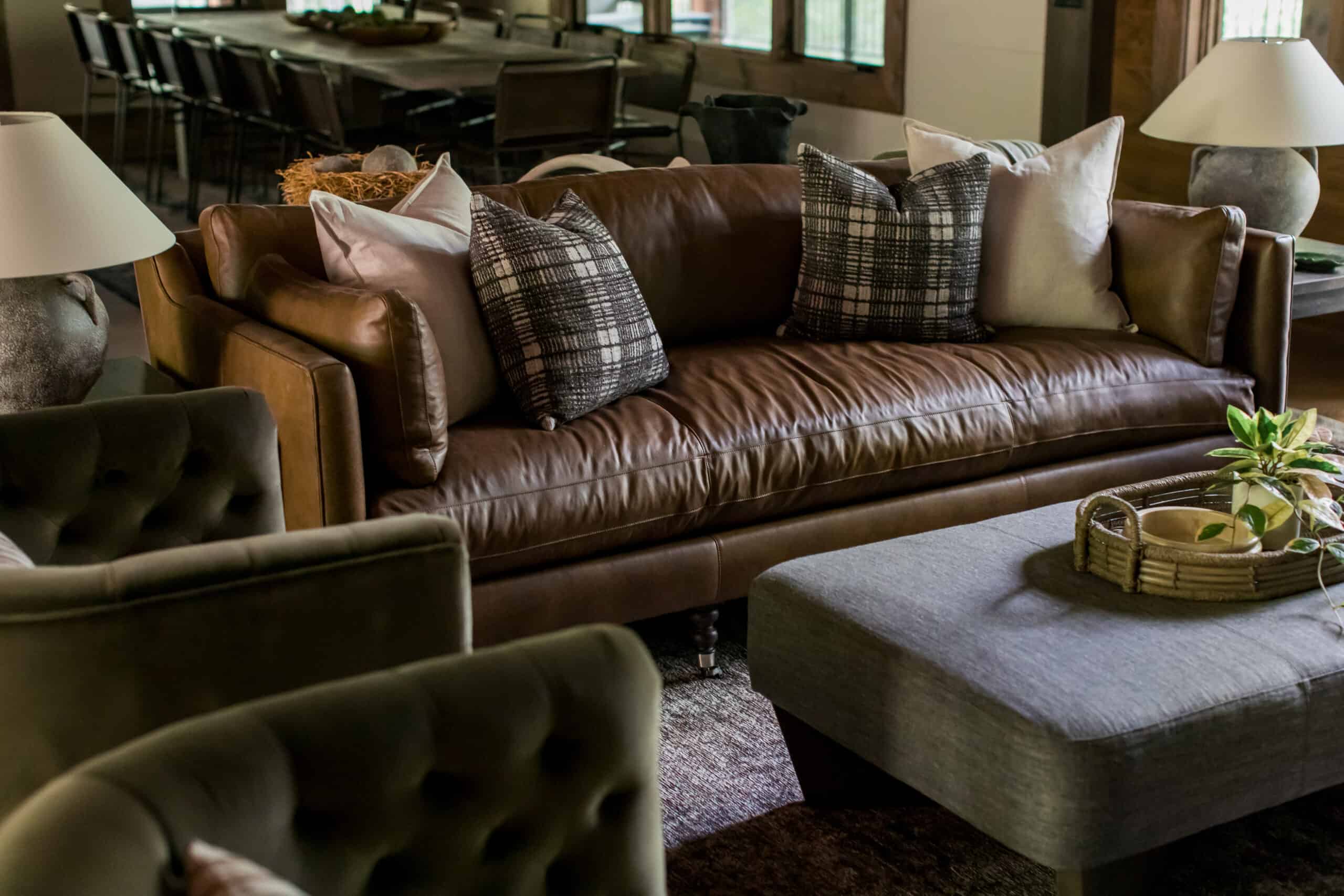 Living room with leather couch, plaid pillows, green velvet chairs, and linen ottoman.