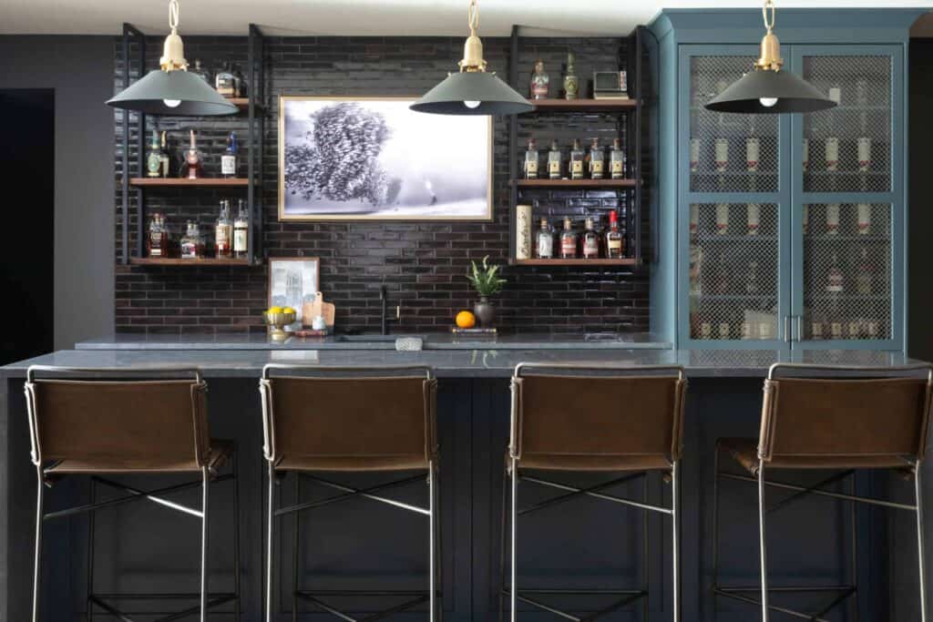 Blue basement bar with brown leather chairs, blue pendant lights, and shelves of liquor.