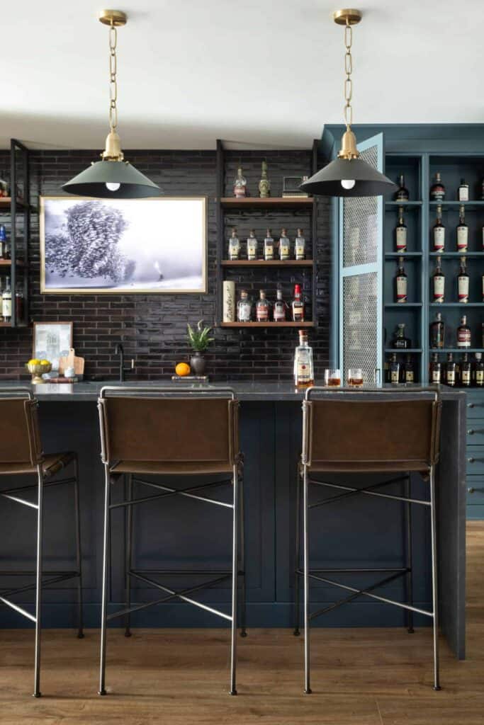 Blue basement bar with brown leather chairs, blue pendant lights, and shelves of liquor.