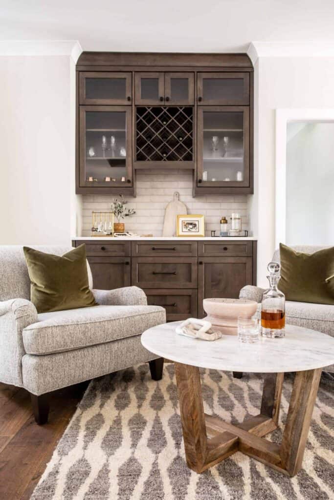 Cozy hang-out area with gray chairs, round marge table, and built-in wood bar and wine rack.
