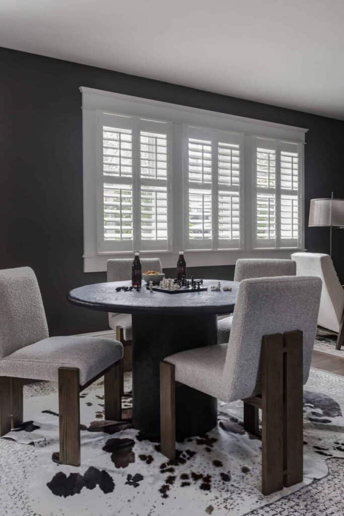 Black concrete table with three gray and wood chairs around it, sitting on a cowhide rug.