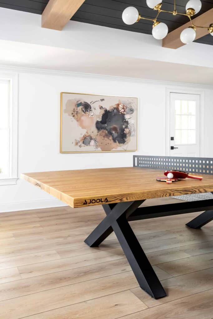 Room with wood floors, black and wood ping pong table, and pink and blush abstract art on the wall.