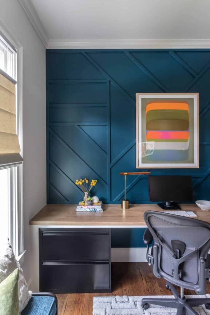 Office with blue accent wall, black office chair, and orange, pink, and green abstract art.