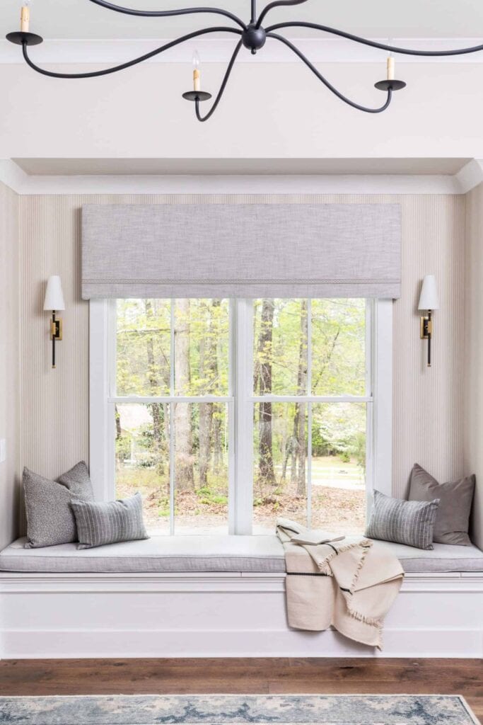 Window nook with built-in bench, gray pillows, and white shade wall sconces.