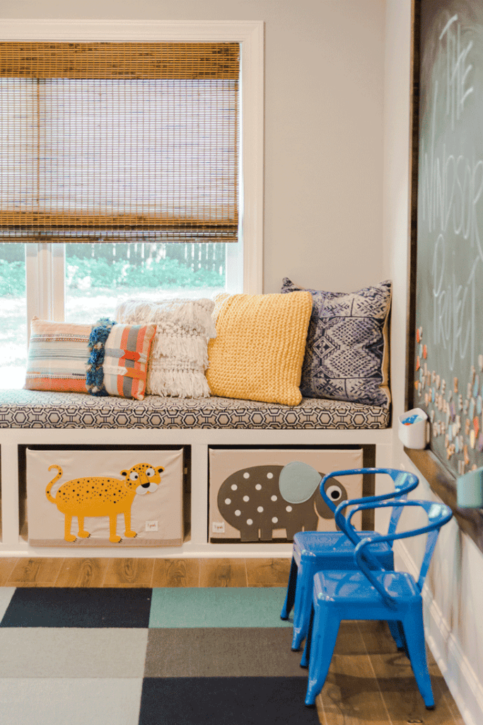 Kid's playroom with blue chairs, drawers with animals, chalkboard, and colorful pillows.