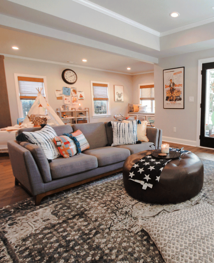 Living room with gray couch, patterned rug, round ottoman, and graphic art.