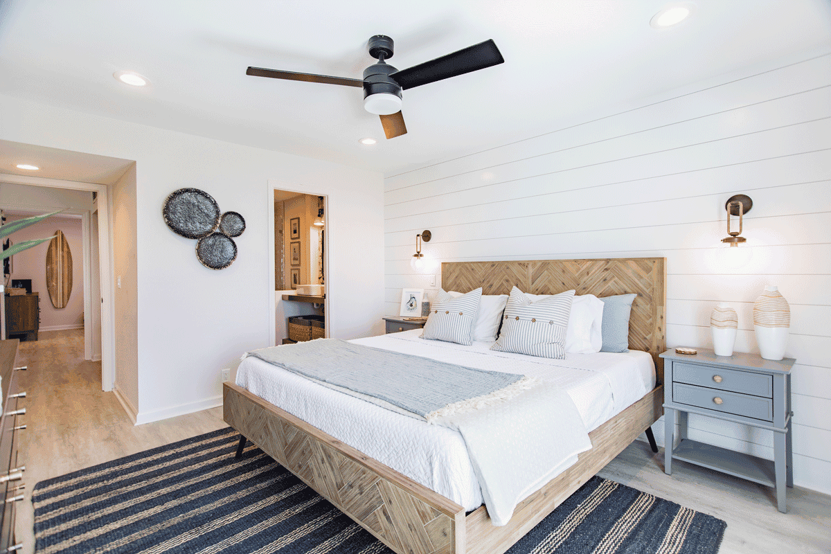 White bedroom with wood frame, striped black rug, and blue furniture.