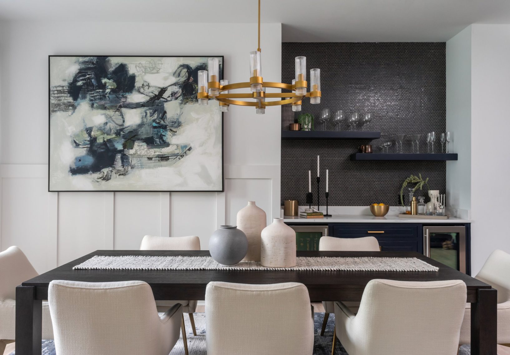 Modern dining room with a dark wooden table with eight white fabric dining room chairs. Brass modern chandelier and a wet bar.