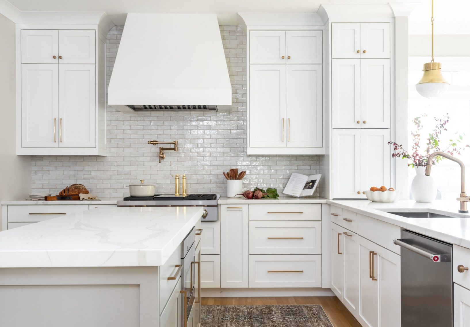 Modern white kitchen with gold hardware, white cabinets, and white hood.